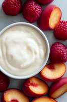 Fresh ripe raspberries and sliced nectarines arranged around white creamy yogurt in ceramic bowl on gray background, overhead view for food photography.