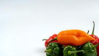 Fresh colorful hot chili peppers including orange habanero and green varieties arranged on white background for culinary and cooking projects.