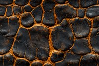 Dramatic black and orange cracked surface pattern with glowing lava-like effect between dark stone shapes creates abstract textural background for design projects.