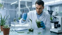 Male scientist in white lab coat and blue gloves conducting botanical research with plant samples and microscope in modern laboratory setting.