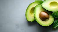 Fresh ripe avocado cut in half with pit and green leaves on gray background, healthy food ingredient for cooking salads and sandwiches.