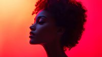 Young African American woman with natural curly afro hair in profile against vibrant red and orange gradient background, eyes closed in serene expression.