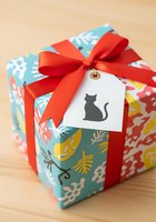 Colorful gift box wrapped in floral patterned paper with bright red ribbon bow and white gift tag featuring black cat silhouette on wooden surface for holiday celebrations.