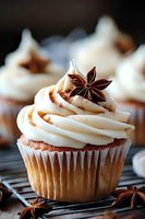 Vanilla cupcake with creamy white frosting swirl topped with star anise and cinnamon dust on cooling rack, macro food photography with selective focus.