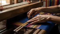 Skilled artisan hands weaving colorful threads on traditional wooden loom creating handmade textile fabric in workshop studio for craft production.