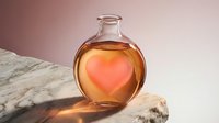Glass bottle with glowing heart inside on marble surface against pink gradient background for romantic wellness and love potion concept designs.