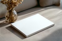 White blank notebook mockup on beige textile surface with dried flowers in glass vase and natural sunlight creating soft shadows, minimal style.