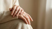 Woman applying moisturizer cream on hands skincare routine self-care wellness beauty treatment soft natural lighting beige sweater comfort.