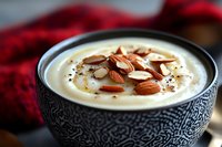Creamy cauliflower soup garnished with toasted sliced almonds and black pepper in decorative ceramic bowl against dark background with red textile.