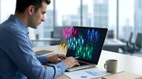 Professional businessman analyzing colorful data visualization charts on laptop computer in modern office environment for financial market research.