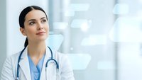 Young female doctor with stethoscope in white coat looking up thoughtfully in modern hospital setting with bright medical facility background.