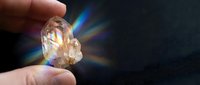 Hand holding raw citrine crystal with light refracting through facets creating rainbow prism effect on dark background. Suitable for wellness, spirituality, and gemstone content.