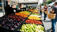 Vibrant farmers market produce stand displaying colorful fresh vegetables and fruits in organized bins with shoppers browsing healthy organic food options.
