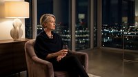 Middle-aged woman with blonde hair in professional attire sitting in modern high-rise apartment at night, gazing at city skyline through floor-to-ceiling windows, warm lamp lighting, contemplative mood for corporate, lifestyle, and editorial use.