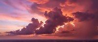 Dramatic sunset cloudscape with vibrant pink and orange hues over ocean horizon. Spectacular sky formation for nature backgrounds and peaceful scenes.