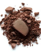 Broken pieces of dark chocolate and cocoa powder scattered on white background, macro shot showing rich texture and detail for culinary and confectionery designs.