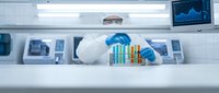 Scientist in protective gloves analyzing colorful test tubes in modern laboratory with digital monitors displaying data charts for research and development.