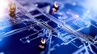 Circuit board close up with electronic components and pathways illuminated in blue technological glow, showing intricate semiconductor design patterns and connections.