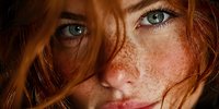 Young redhead woman with freckles and green eyes in warm golden light. Natural beauty portrait with soft lighting and intimate close-up composition.