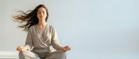 Young woman with flowing hair meditating in lotus position wearing beige outfit against white background. Peaceful mindfulness practice for wellness and relaxation.