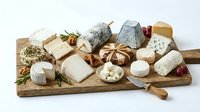 Assorted artisanal cheeses with fresh herbs and nuts arranged on wooden board, perfect for food styling, culinary content, gourmet dining, and restaurant menus.