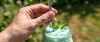 Young adult male hand holding straw in glass of refreshing mint water with ice cubes outdoors. Beverage and hydration concept for summer drinks and wellness.