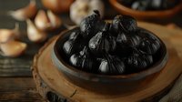 Black fermented garlic bulbs in ceramic bowl on wooden board, with fresh garlic cloves in background for culinary contrast.