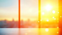 Blurred sunset cityscape with bright sun and bokeh lights reflecting on wooden surface, creating warm atmospheric mood for background designs and presentations.