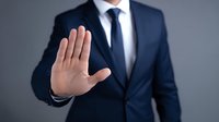 Businessman in navy suit showing stop gesture with palm forward, representing boundary setting or rejection in professional context.