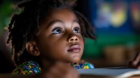 Young African girl with natural hair gazes upward with wonder and curiosity, illuminated by soft dramatic lighting that highlights her expressive eyes and innocent expression.