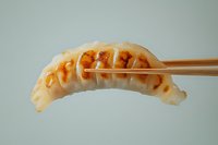 Grilled dumpling with golden filling held by wooden chopsticks against minimal background, showcasing Asian cuisine delicacy.