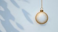 Elegant gold Christmas ornament with white glitter hanging against soft blue wall with window shadow patterns.