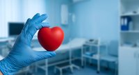 Medical professional in blue gloves holding red heart in modern hospital setting for cardiology healthcare and heart disease prevention concepts.