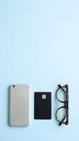 Smartphone, black credit card, and tortoise shell glasses arranged on a light blue background with copy space for finance or lifestyle.