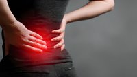 Person suffering from lower back pain with red glow highlighting the affected area against dark background, illustrating common health condition.