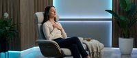 Young Asian woman relaxing in modern massage chair at luxury spa wellness center with ambient lighting and tropical plants for stress relief.