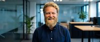 Happy mature Caucasian businessman with beard smiling in modern office workspace for corporate leadership and professional success concepts.