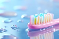 Pink toothbrush with colorful bristles on wet blue surface with water droplets, creating reflection for dental hygiene and oral care concept.