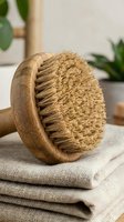 Natural bamboo dry body brush with coconut fiber bristles on linen towels for exfoliating skincare routine and spa wellness treatments at home.