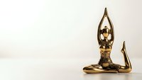 Golden bronze figurine of woman in yoga meditation pose with hands raised above head on neutral background for wellness and mindfulness concepts.