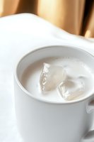White ceramic cup filled with creamy liquid and ice cubes, soft focus background creates elegant minimalist composition for beverage and lifestyle content.