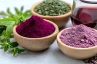 Vibrant natural food coloring powders in wooden bowls - purple acai, green spirulina, and pink dragon fruit. Fresh herbs and berry juice complement organic ingredients.