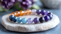 Colorful chakra bracelet with natural gemstone beads arranged in rainbow order on stone surface, featuring amethyst, aquamarine, and amber crystals for meditation and healing.