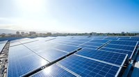 Large solar panel installation on rooftop with city skyline and blue sky background showcasing renewable energy technology for sustainable power generation.