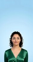 Young woman with curly dark hair and olive complexion wearing emerald green wrap top against light blue background for professional headshot or corporate portrait use.