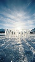 Word WINTER sculpted from ice stands on a frozen lake with snowy mountains and sunlit sky, evoking cold season atmosphere.