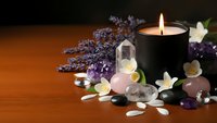 Spa wellness scene with burning candle, healing crystals, lavender flowers and white petals on wooden surface for relaxation and meditation therapy.