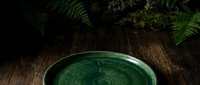 Overhead view of green ceramic bowl on rustic wooden surface with fresh fern leaves, natural lighting for culinary, wellness, and organic product styling.