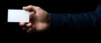 Male hand in dark blue suit holding blank white business card on black background, mockup for branding and corporate identity design.