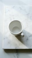 Empty white ceramic mug on marble surface, overhead view. Minimalist kitchen styling with natural light and shadow for beverage, coffee, tea, or product mockup designs.